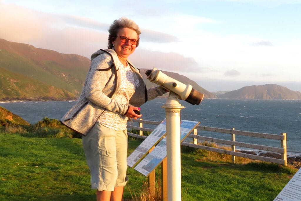 A happy lady with a giant fixed pair of binoculars pointing out to sea.