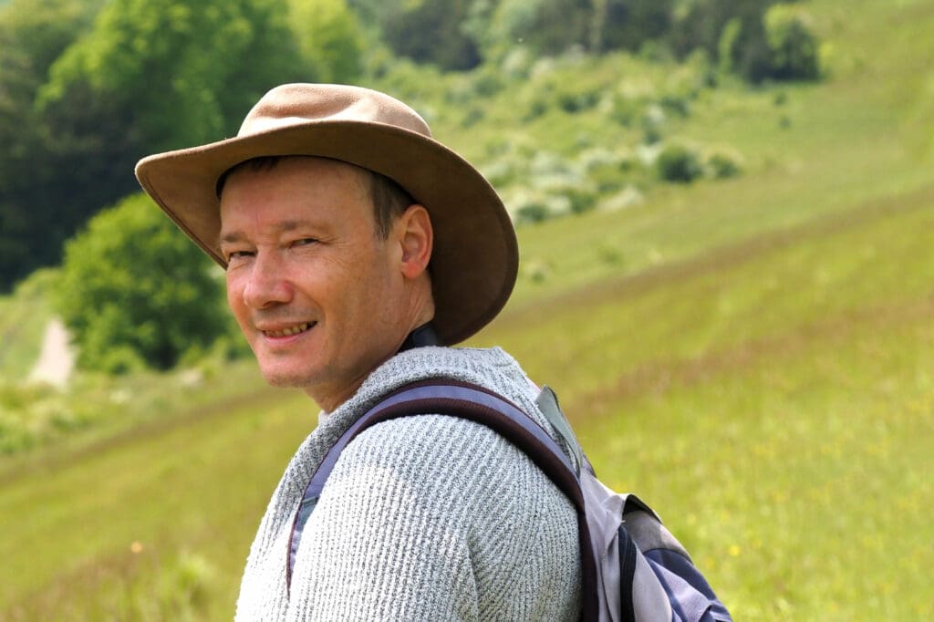 A man wearing a hat in green countryside.