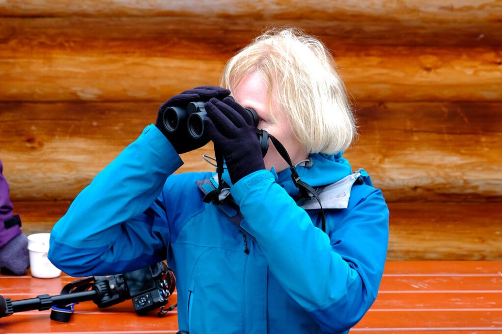 A woman in a blue coat looking through a pair of binoculars.