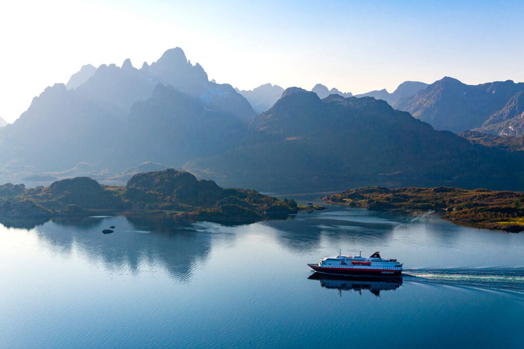 A cruise ship on water with a mountainous landscape behind