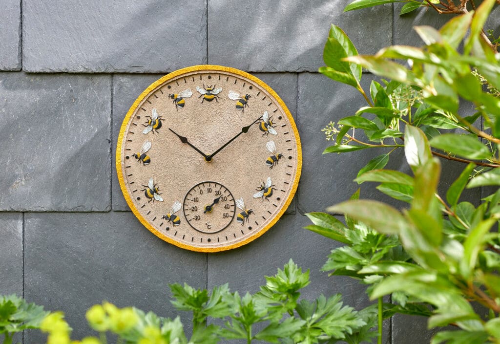 An outdoor clock with thermometer with a bee pattern on a wall.