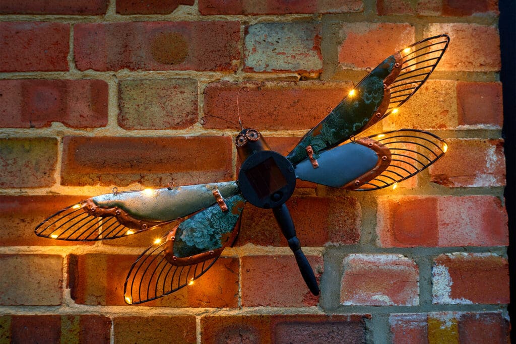 An outdoor wall light shaped like a Dragonfly on a brick wall.