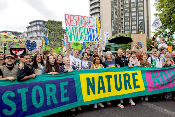 A group of people standing behind a long colourful banner that reads "restore nature now"