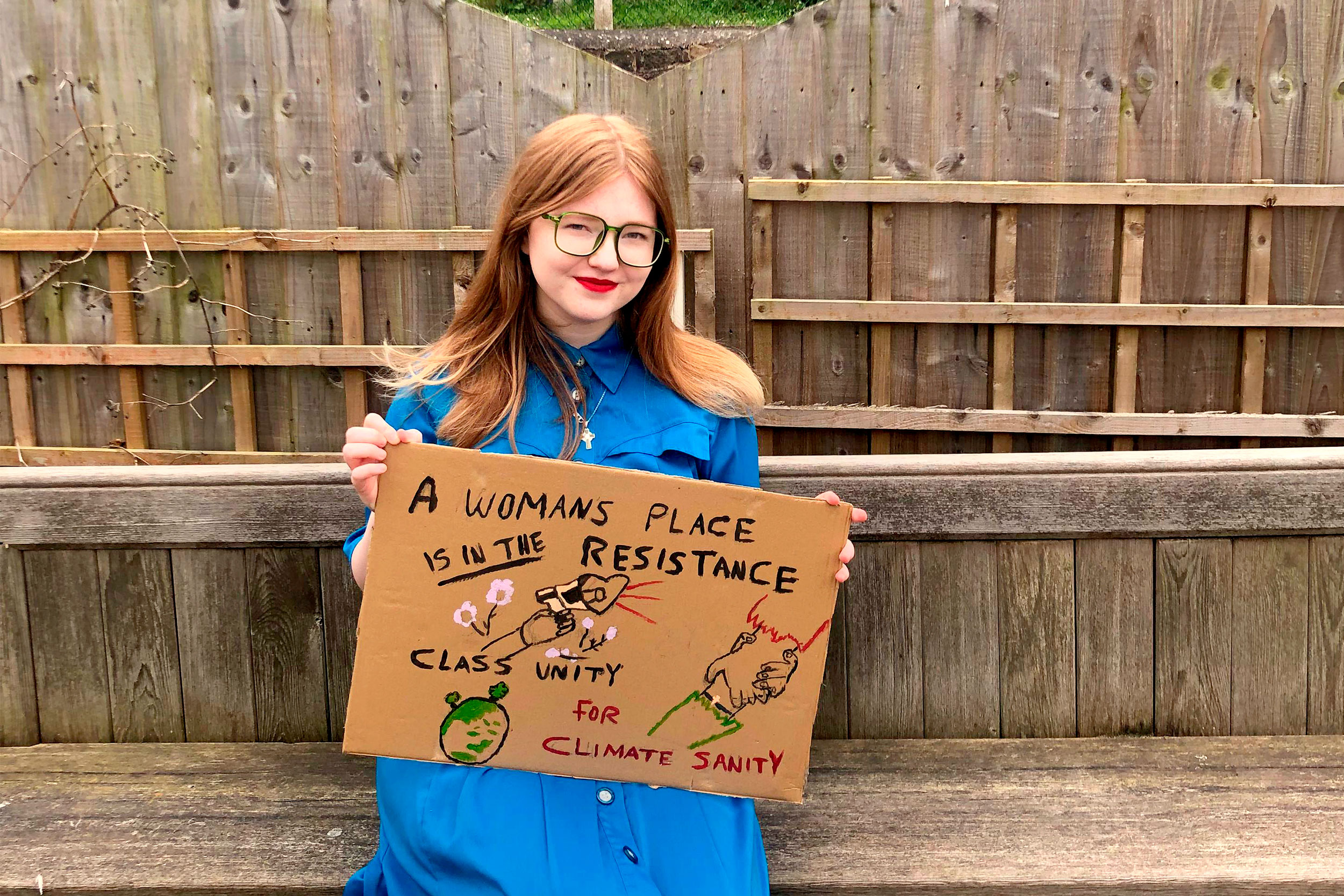 Chelsea Valentine holds up a protest sign while sitting on a bench