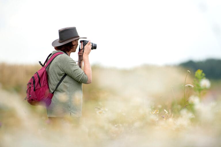 A photographer holds a camera in a hazy field, facing away from the viewer.