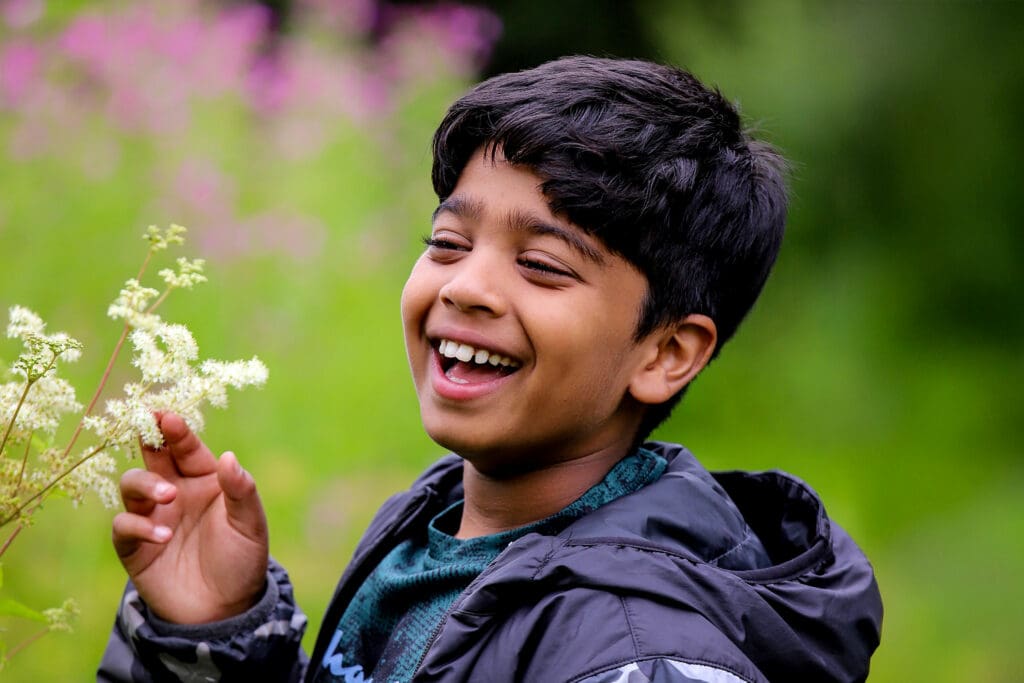 Aneeshwar laughs alongside white flowers on a green background