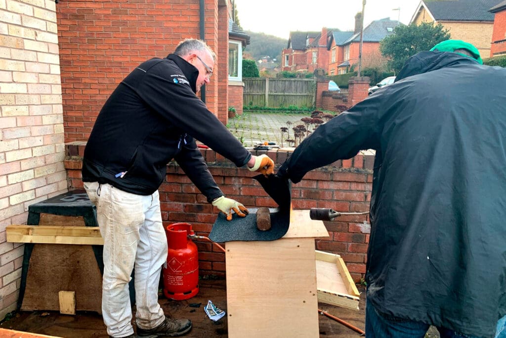 Two people putting a waterproof roof on an owl nestbox.