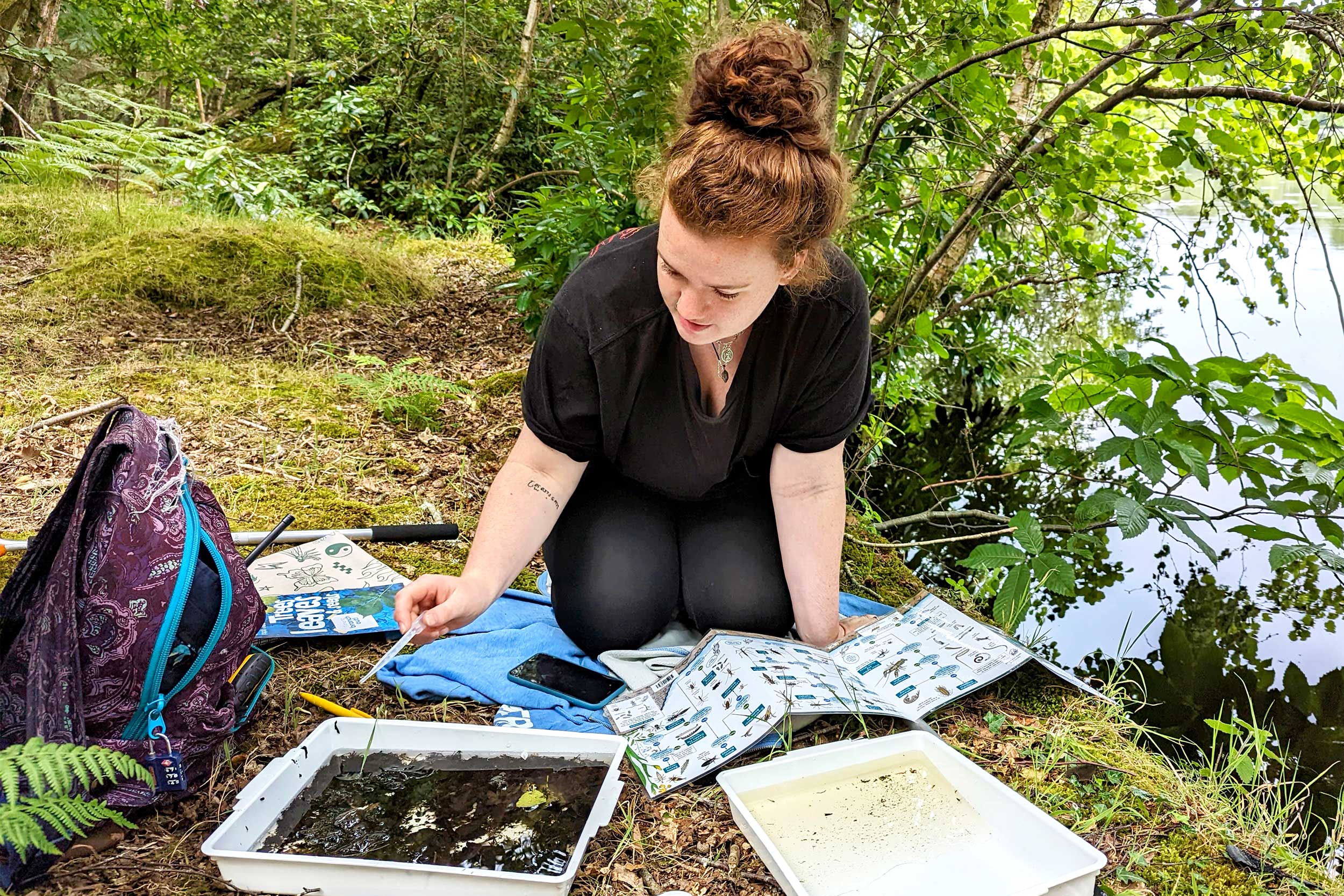 An ecology student sitting with research equipment by a river.