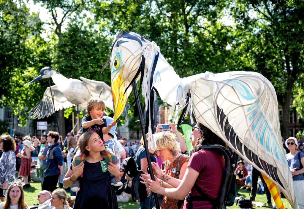 Families at a march with two puppeteers wearing large bird puppets