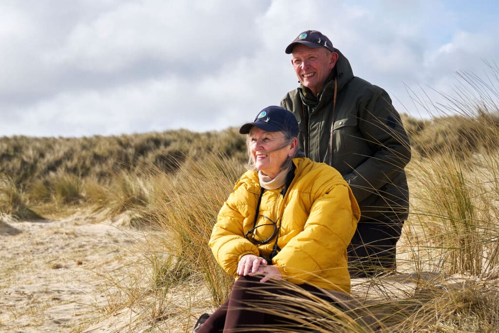 Two people looking out to sea, sitting on a sandy beach