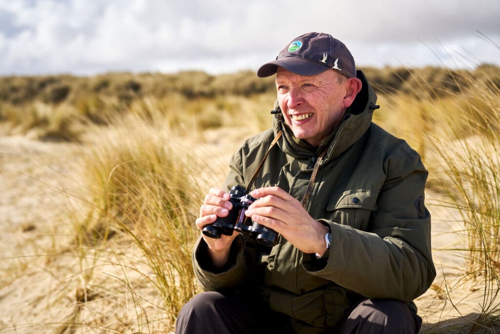 Dave Cook, holding binoculars as he looks out to sea
