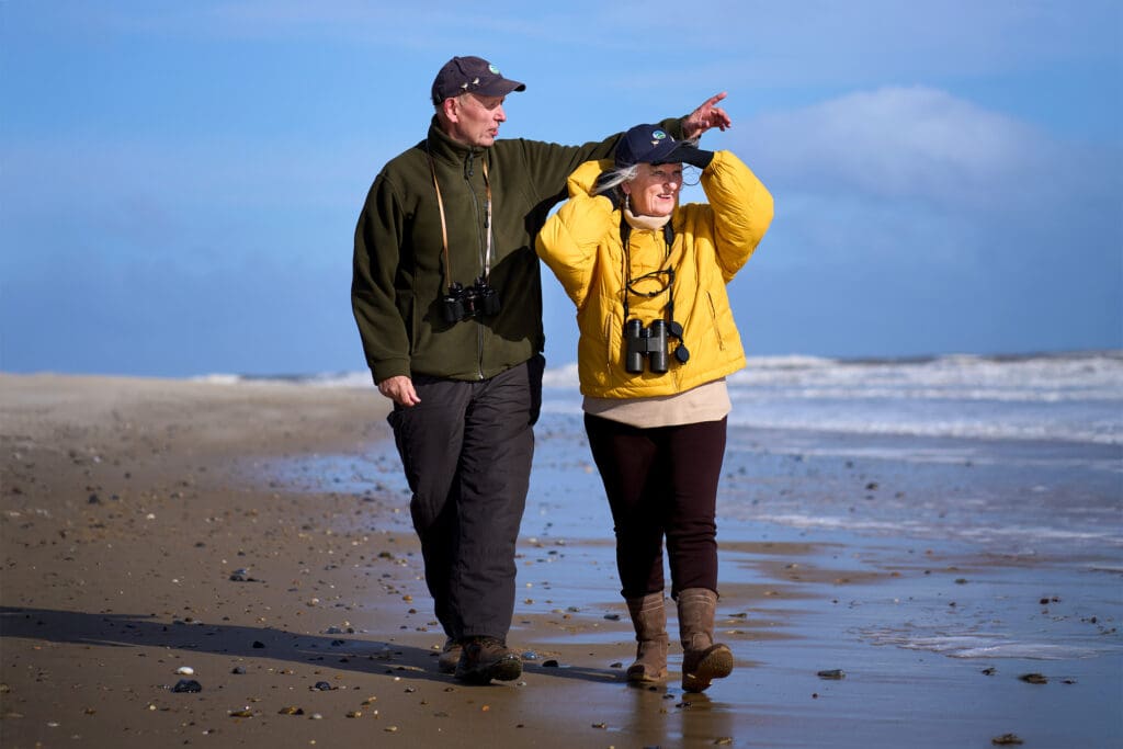 Dave and Jacinta walk along the shore, looking in the same direction out to sea
