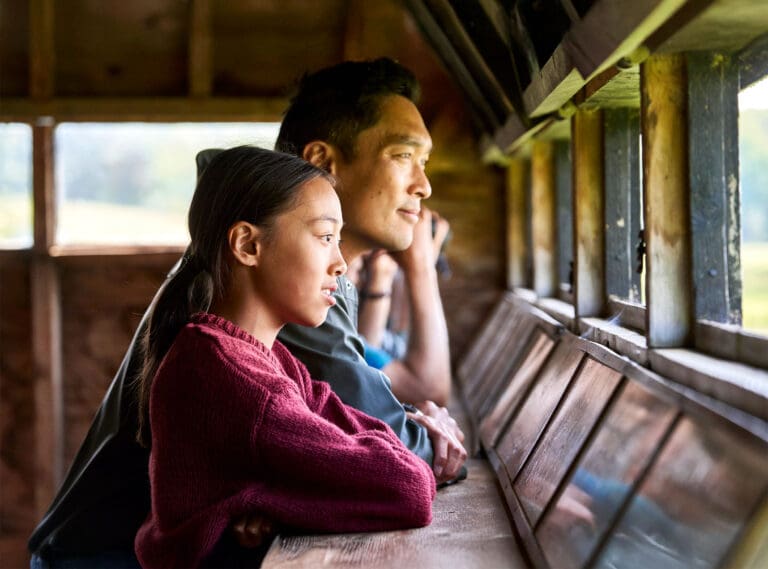 A man and young girl look out from a bird hide