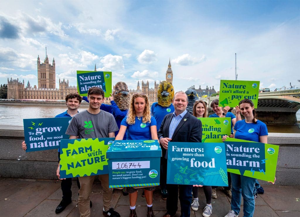 A group of campaigners stand with nature-friendly farming protest signs outside the Houses of Parliament