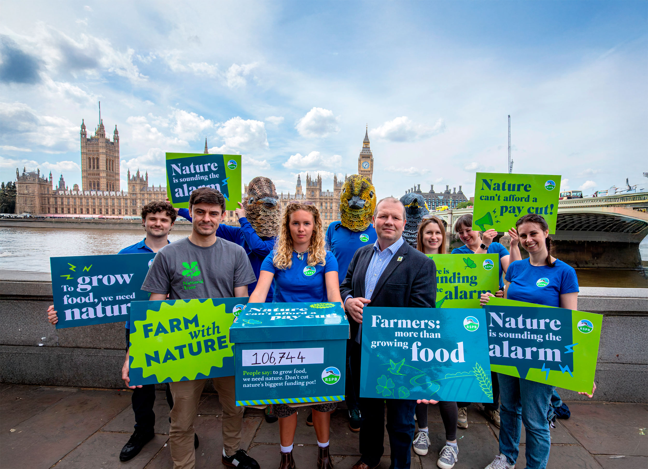 A group of campaigners stand with nature-friendly farming protest signs outside the Houses of Parliament