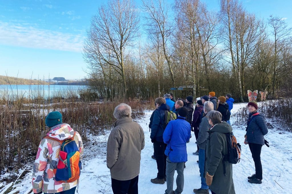A group of people looking out on a lake at an RSPB reserve in the snow