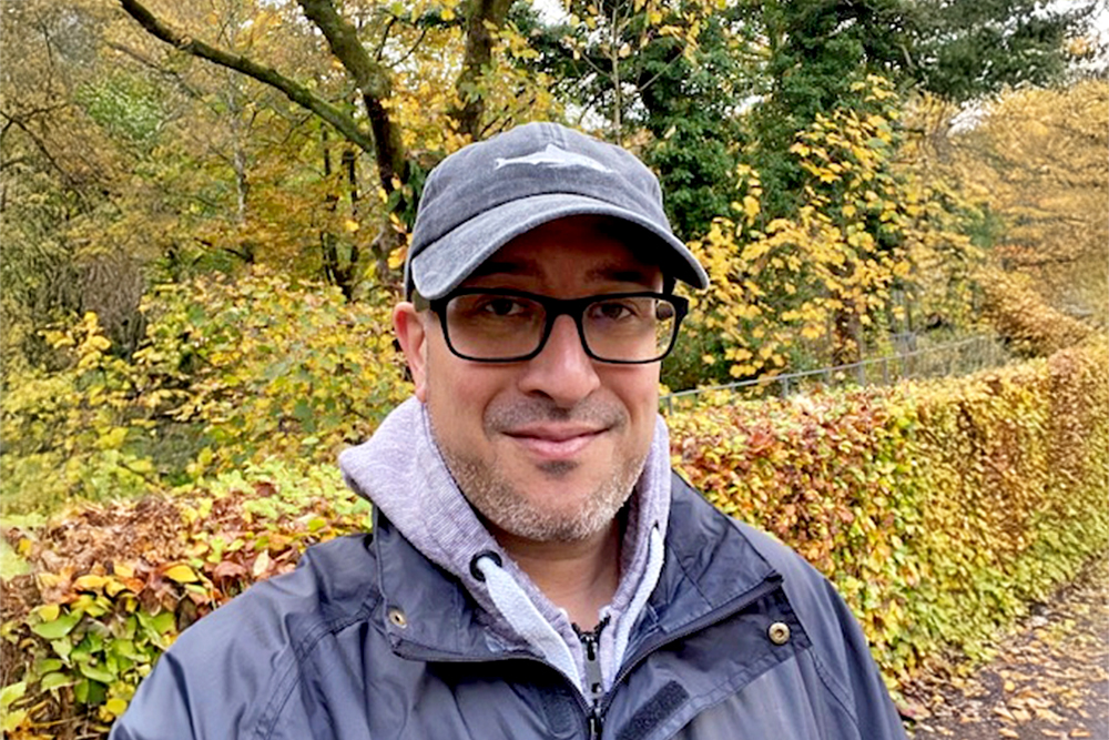 A selfie of Tom Oliver outside with autumnal trees behind him
