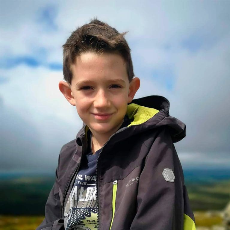 A young boy is sat outside smiling at the camera