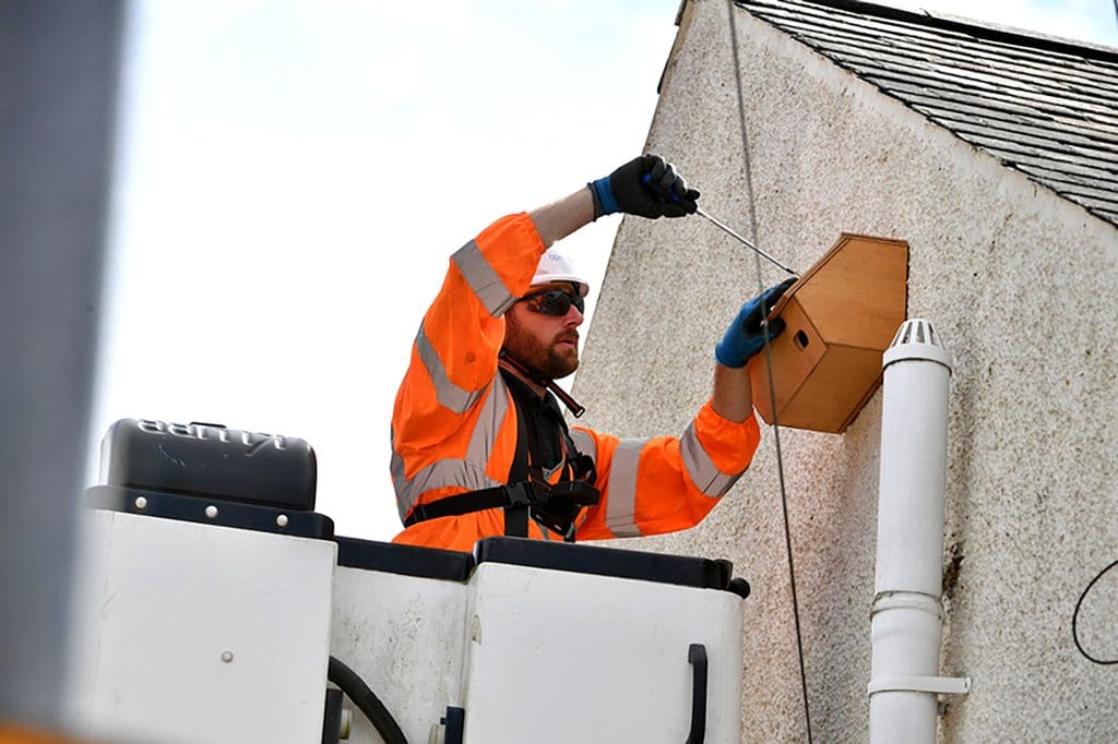 An OpenReach engineer fits a Swift box to the side of a house