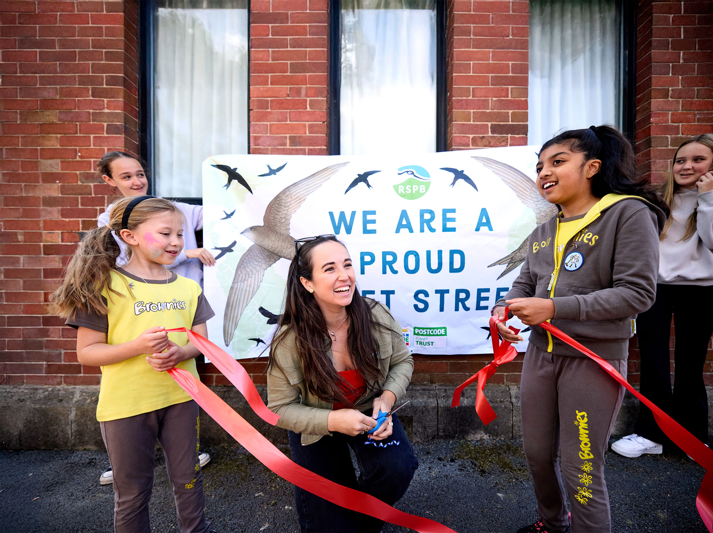 Megan McCubbin with some young Brownies cutting a red ribbon in front of an RSPB sign that reads 'We are a proud Swift Street'