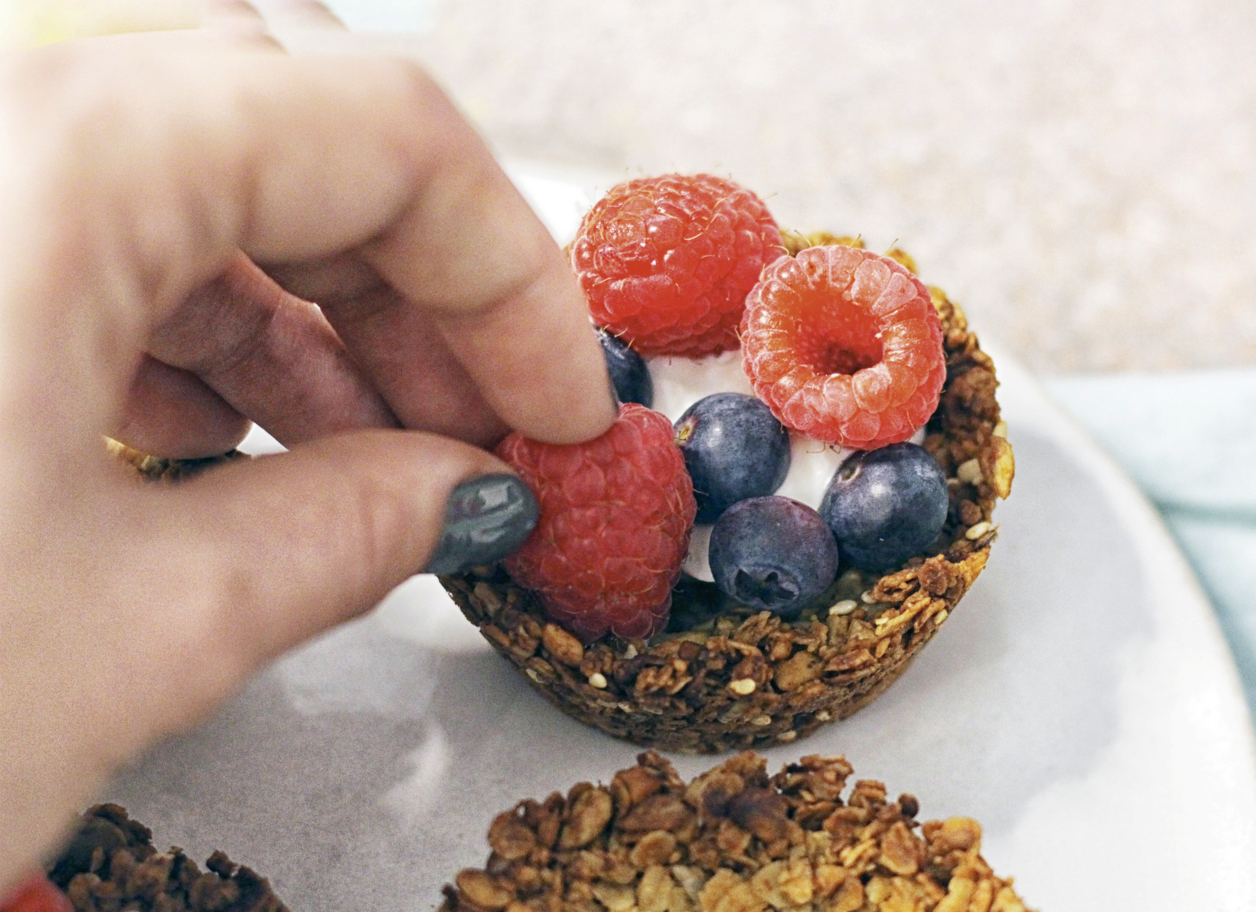 A woman adds a raspberry to the top of a granola muffin