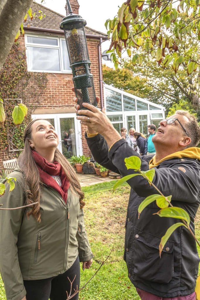 A man and woman hang a bird feeder in a garden