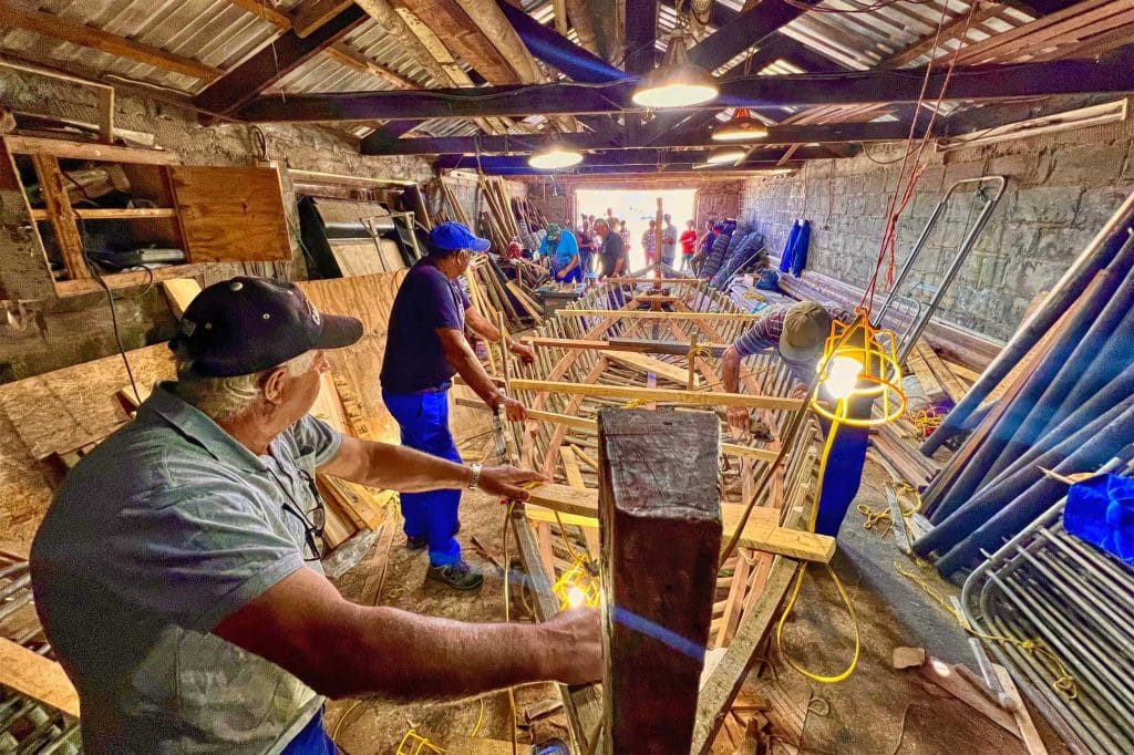 A team of people in an outbuilding working on the wooden frame of a longboat