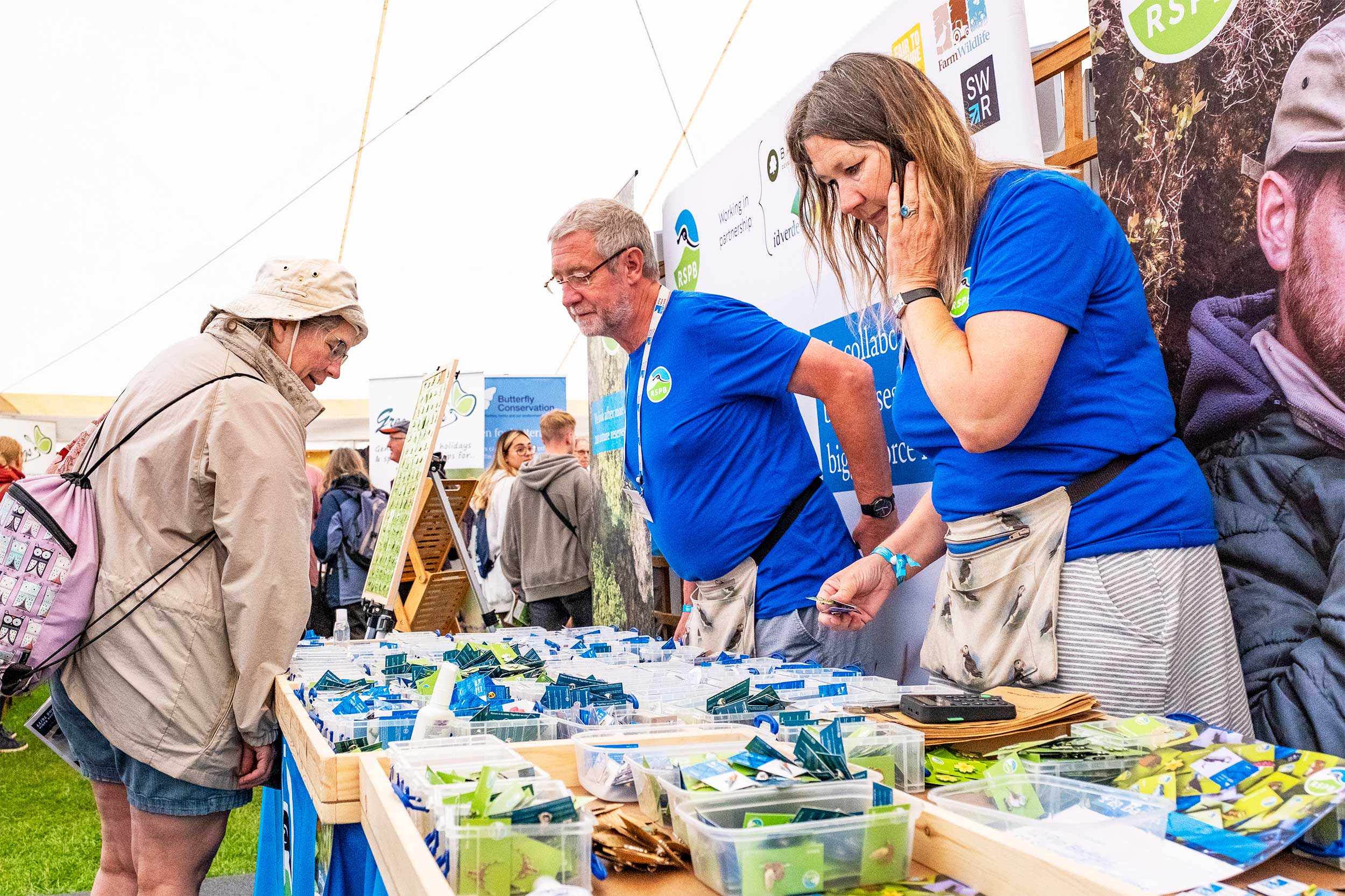 Two RSPB workers stand behind a table full of RSPB pin badges whilst a customer looks through them