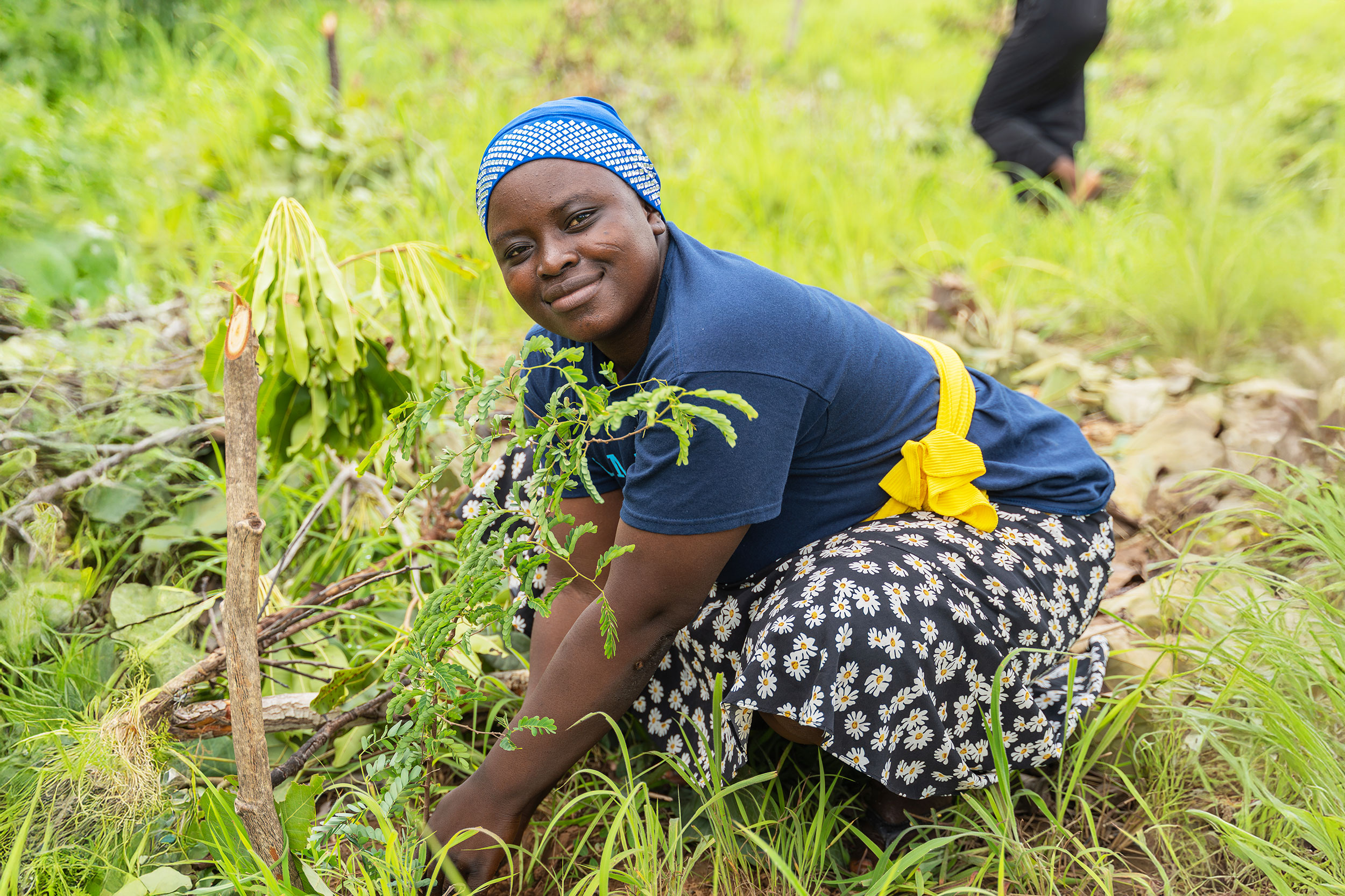 A woman is crouched down planting whilst smiling at the camera