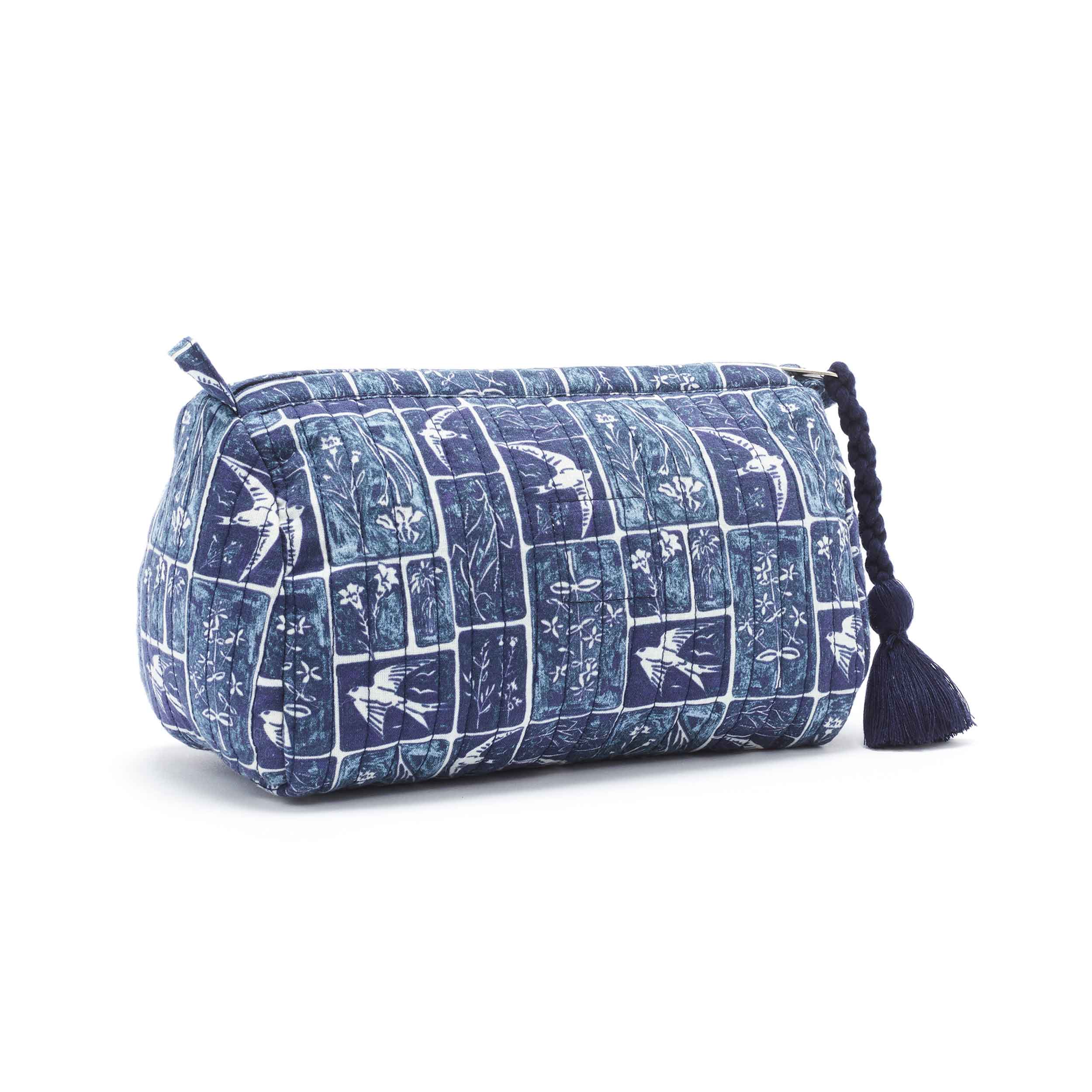 Dark blue and pale cream cosmetics bag, with lino-print-style scenes of swifts and meadow flowers in different-sized squares and rectangles arranged in a linear design. There is a long, dark blue tassel on the end of the zip. The shape of the bag is a triangular prism.