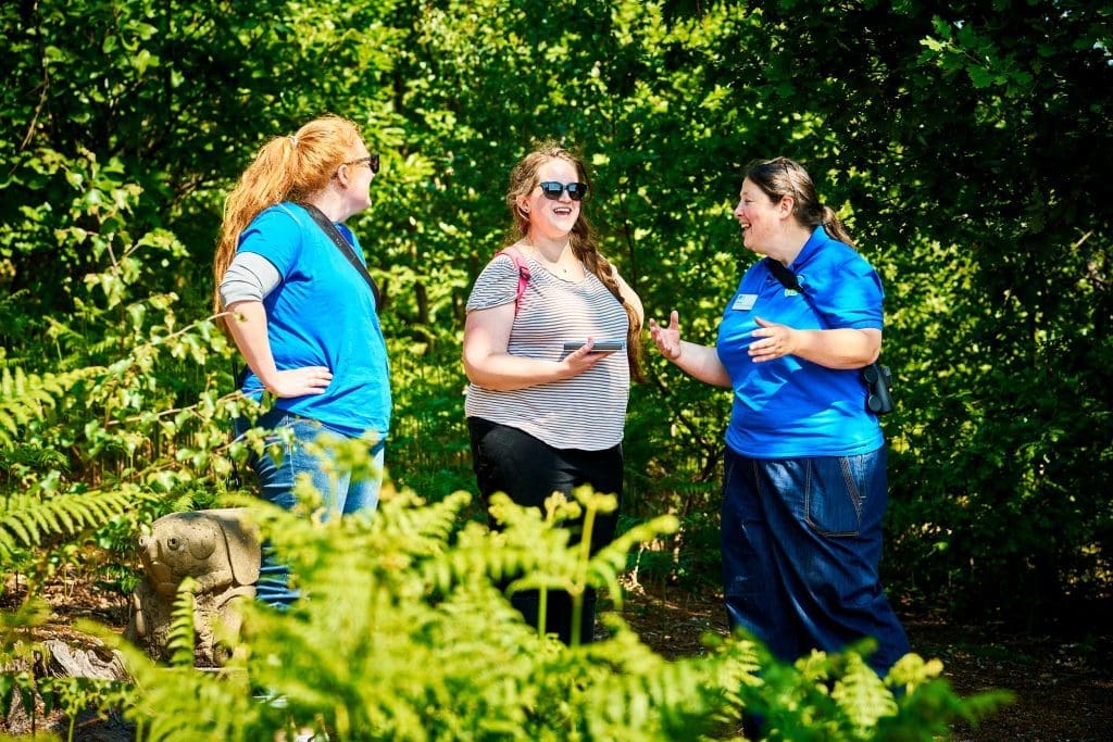 Three women talking and laughing stood amongst trees on a nature reserve