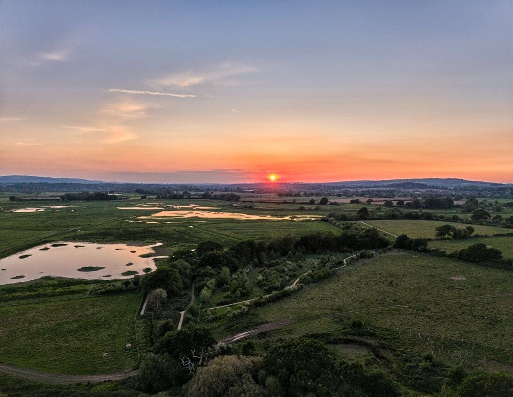 An aerial shot overlooking fields and ponds with the sun setting on the horizon