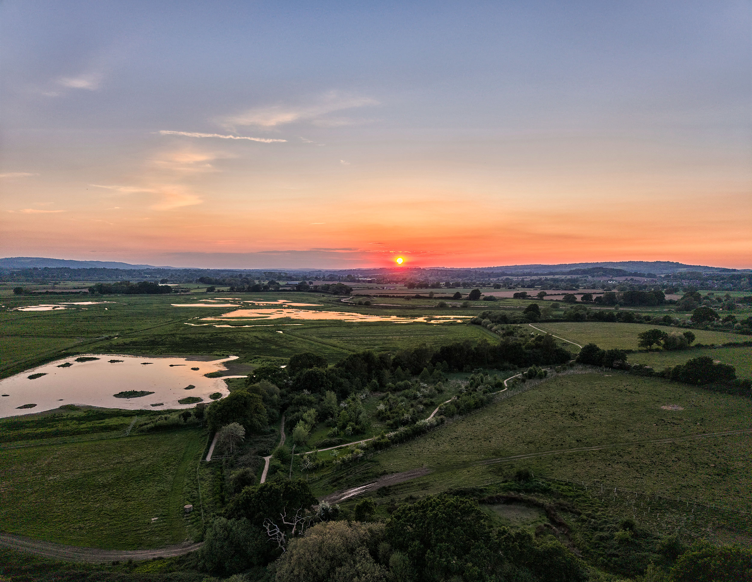 An aerial shot overlooking fields and ponds with the sun setting on the horizon
