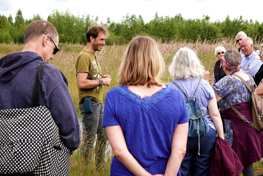 Alwyn stands in the meadow, with people gathered in front of him