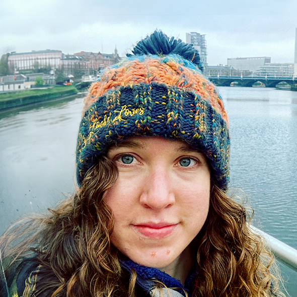 A selfie of a woman standing by a river wearing a colourful bobble hat