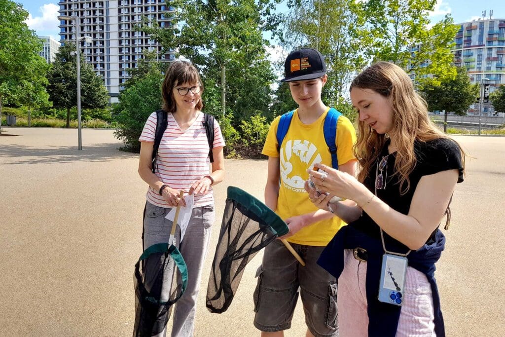 Three people standing in an urban area holding nets on sticks, on a sunny day.