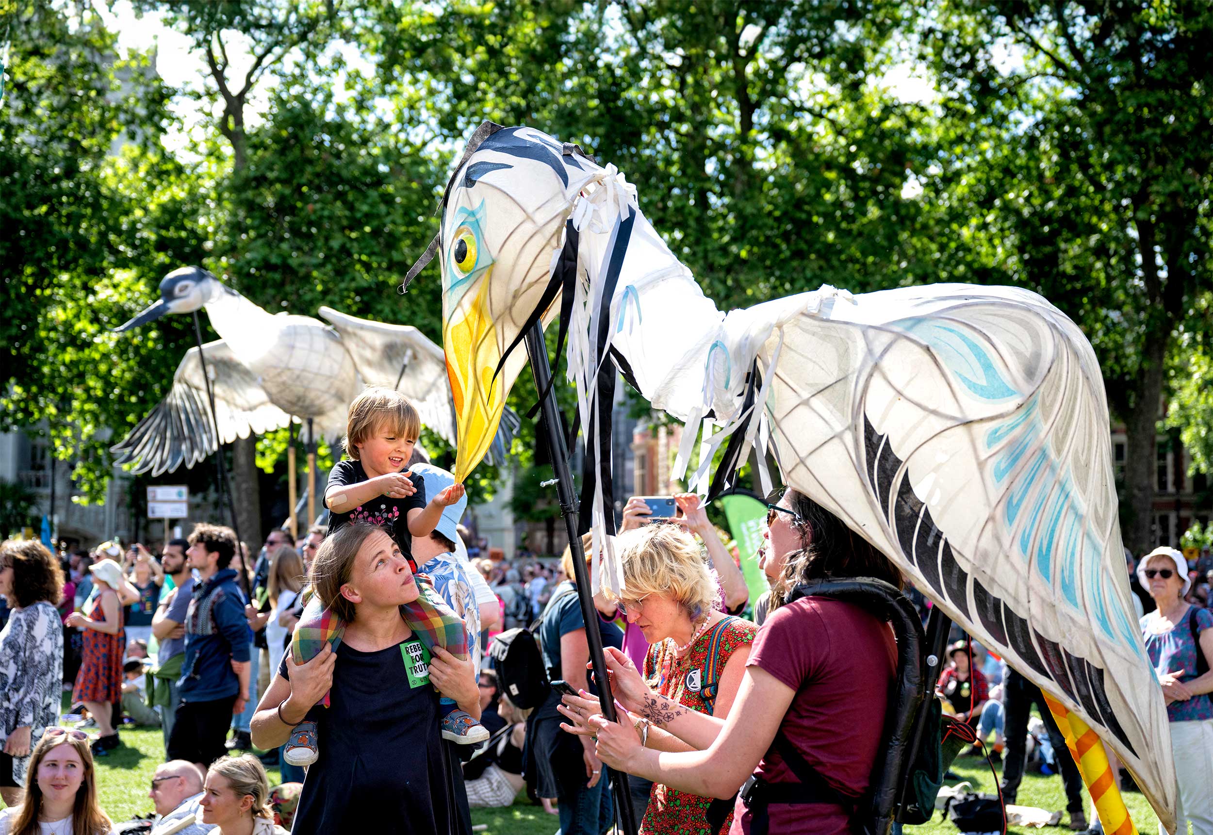 Families at a march with two puppeteers wearing large bird puppets