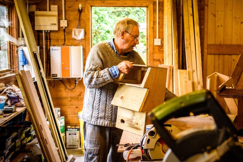 A man is in a workshop surrounded by wood and tools. He is building Swift nest boxes.