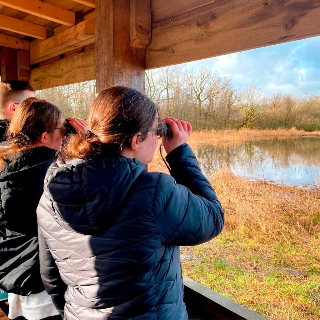 Three people in a hide, looking through binoculars over a lake