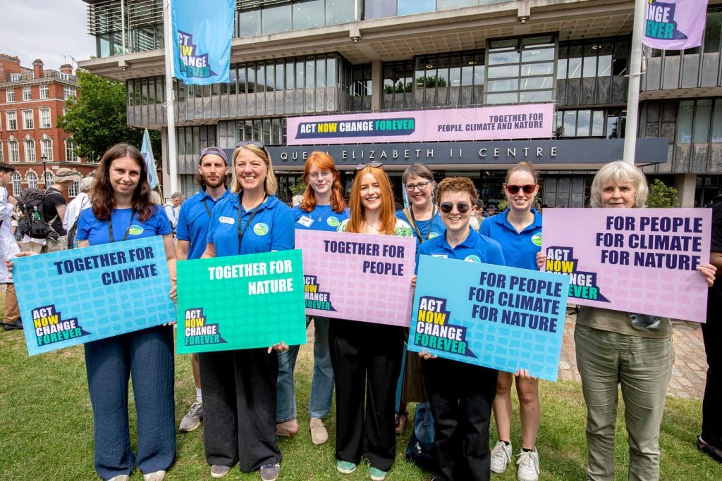 A group of campaigners stand outside the Queen Elizabeth II Centre holding placards with messages about working together to save nature
