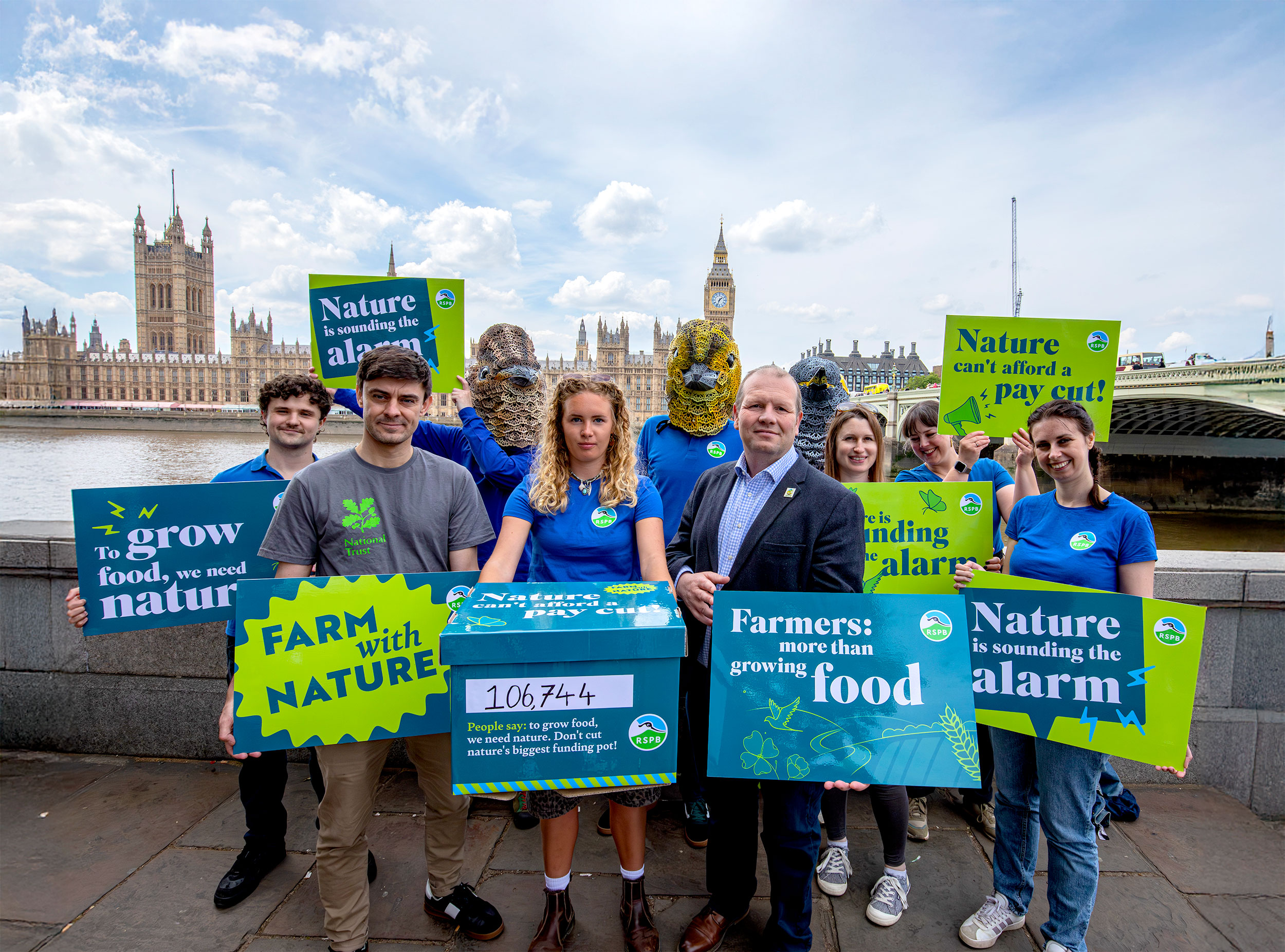 A group of campaigners stand with nature-friendly farming protest signs outside the Houses of Parliament