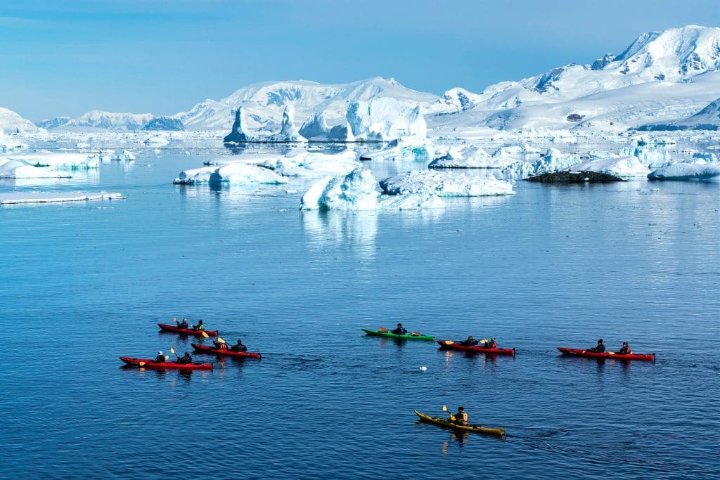 People on brightly coloured kayaks on water in front of icey landscape