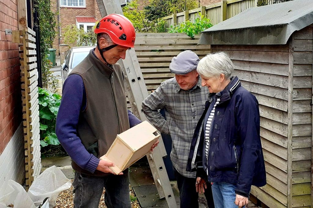 A man wearing a hard hat holds a Swift nest boxing ready for installation whilst a man and woman look over it