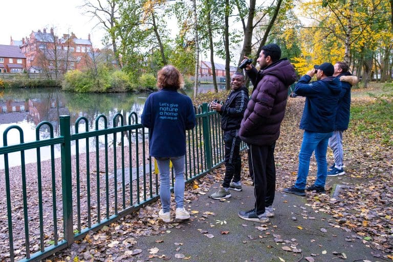 A group on a guided nature walk looking out over a pond in an urban area with binoculars