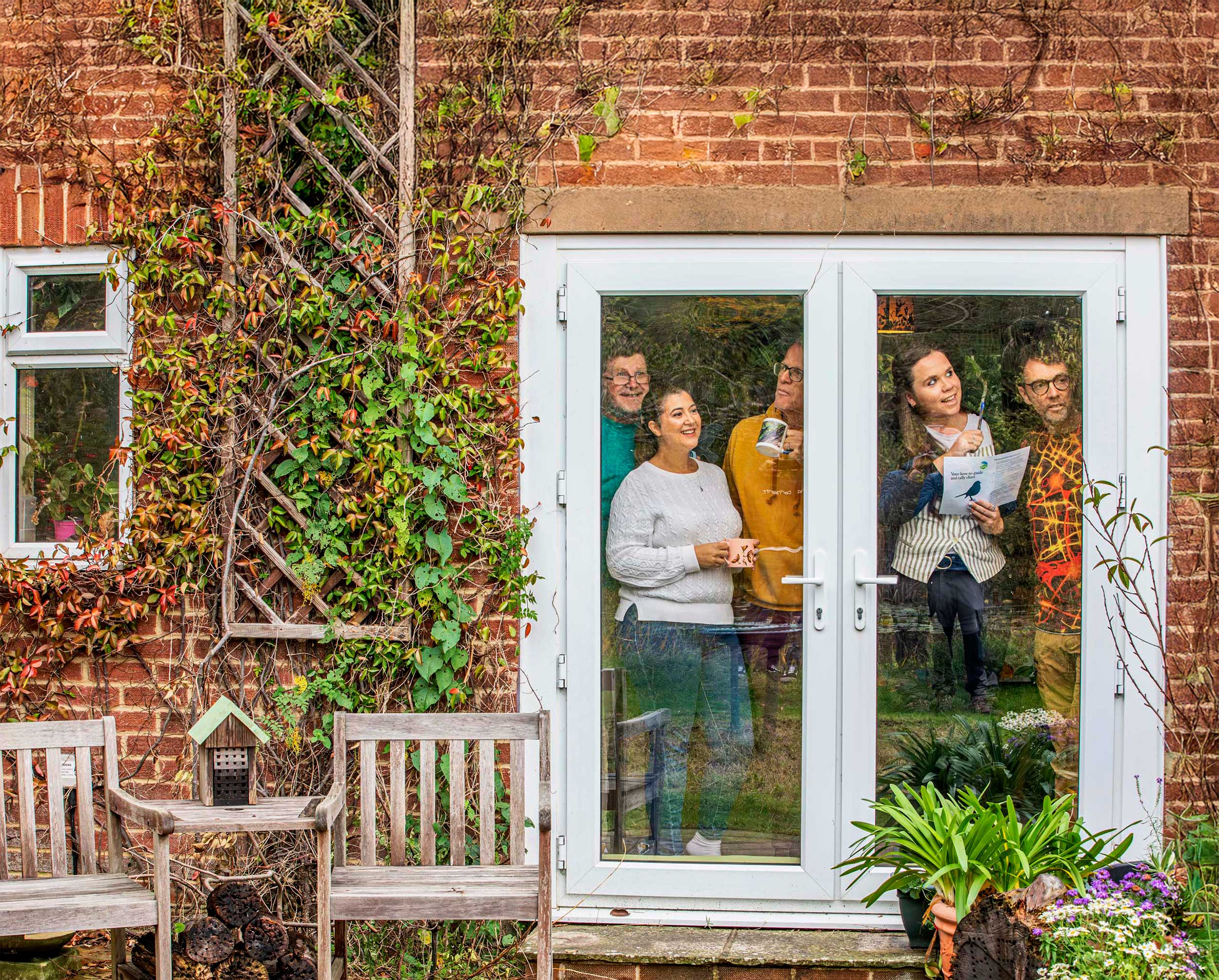 A group of adults birdwatching from inside a house. They are pointing at the sky and smiling
