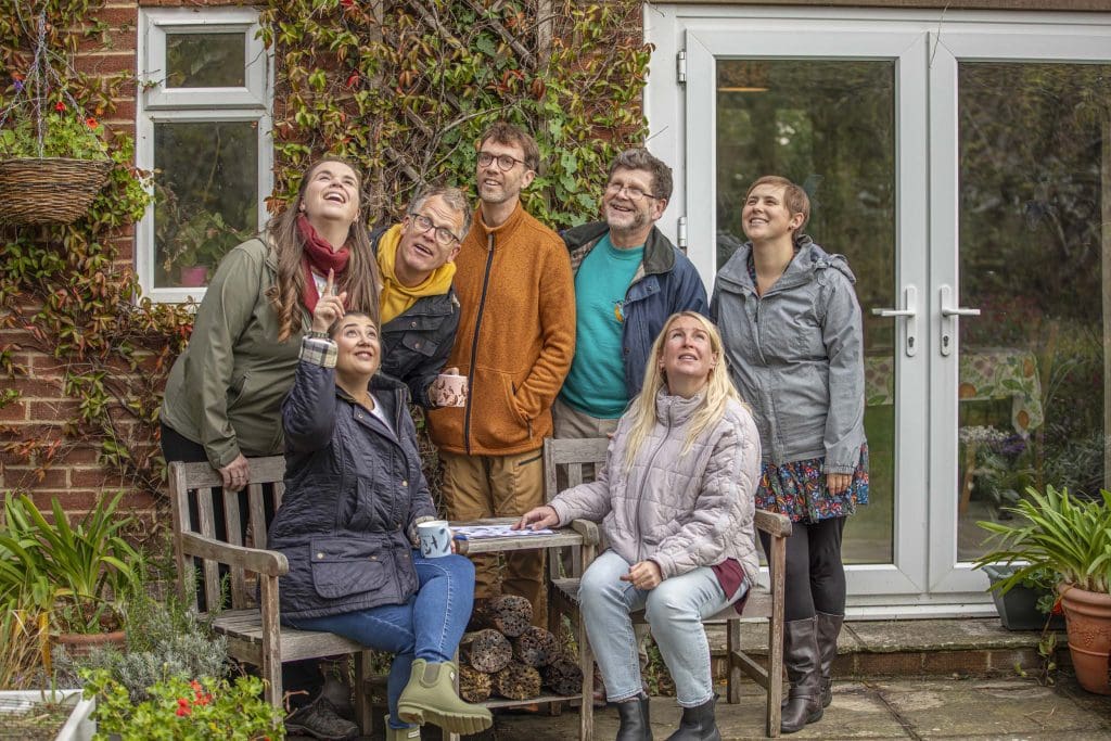 A group of adults outside in a garden birdwatching, looking and pointing at the sky