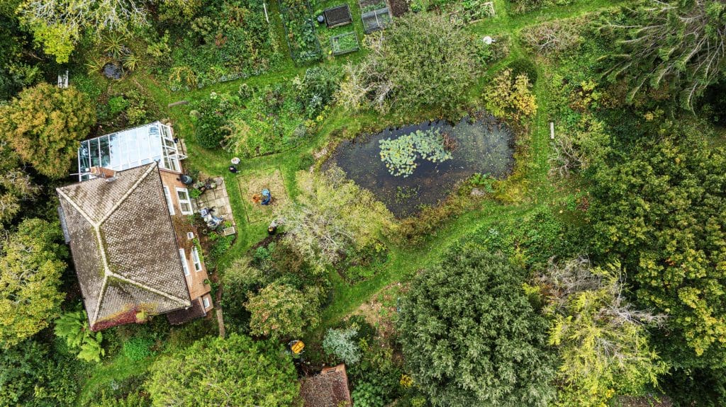An aerial shot of a large house and garden with a pond in the middle and lots of trees