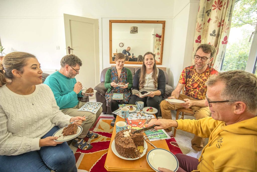 A group of adults sit around a table eating cake and laughing together