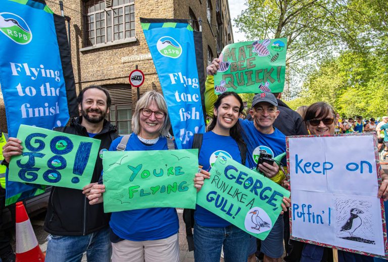 RSPB volunteers and supporters at the 2026 London Marathon, holding up posters with messages such as 'George, run like a Gull', Keep on Puffin' and 'Go Jo Go'.
