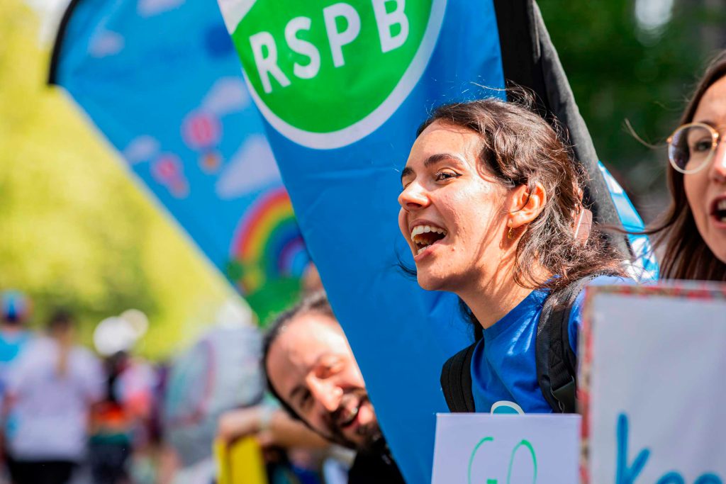 IMAGE.RSPB-staff-and-volunteers-cheering.RSPB_1004291.Credt-BenAndrew A male and female cheering on runners from the sidings, surrounded by RSPB banners
